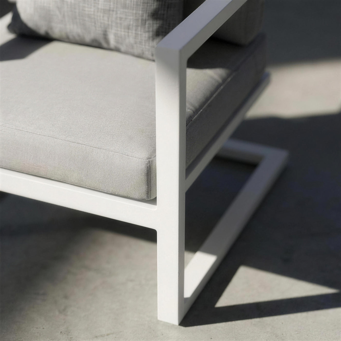 Detalle del brazo plano blanco del sillón y su base voladiza de aluminio, con la sombra dura del sol andaluz