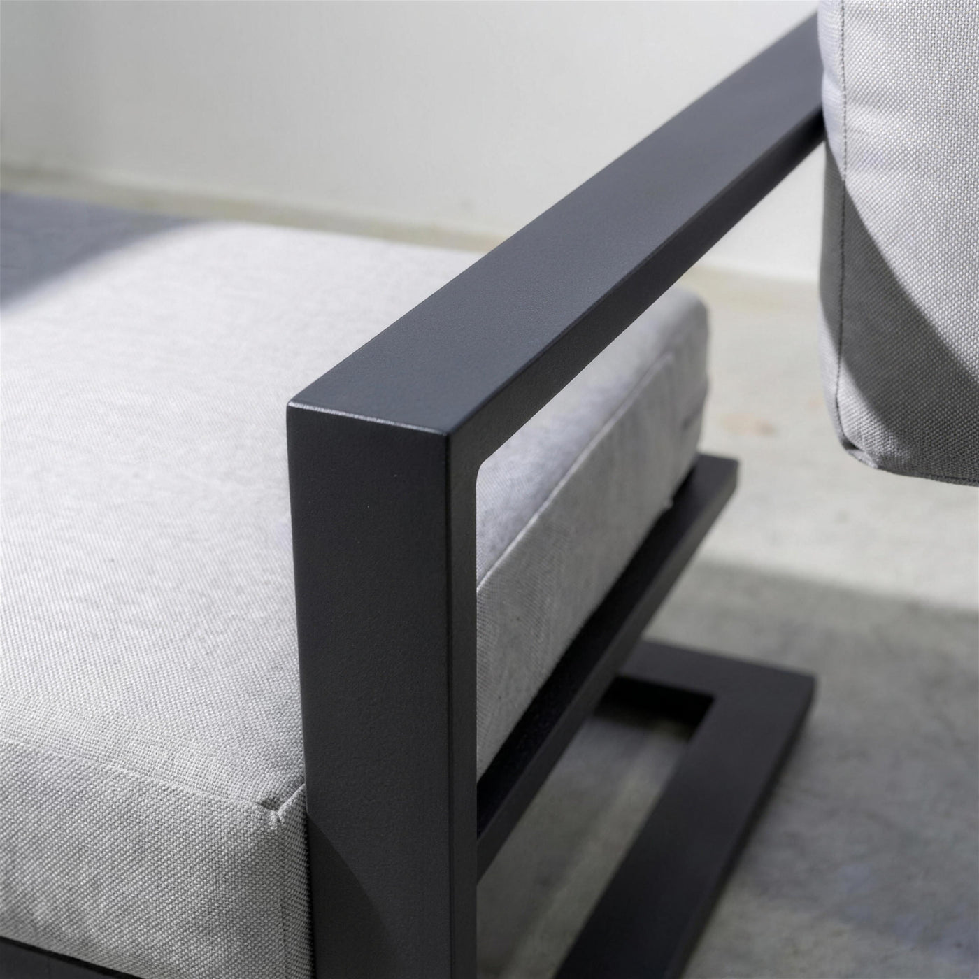 Detalle del brazo plano antracita del sillón y su base voladiza de aluminio, con la trama del cojín gris claro