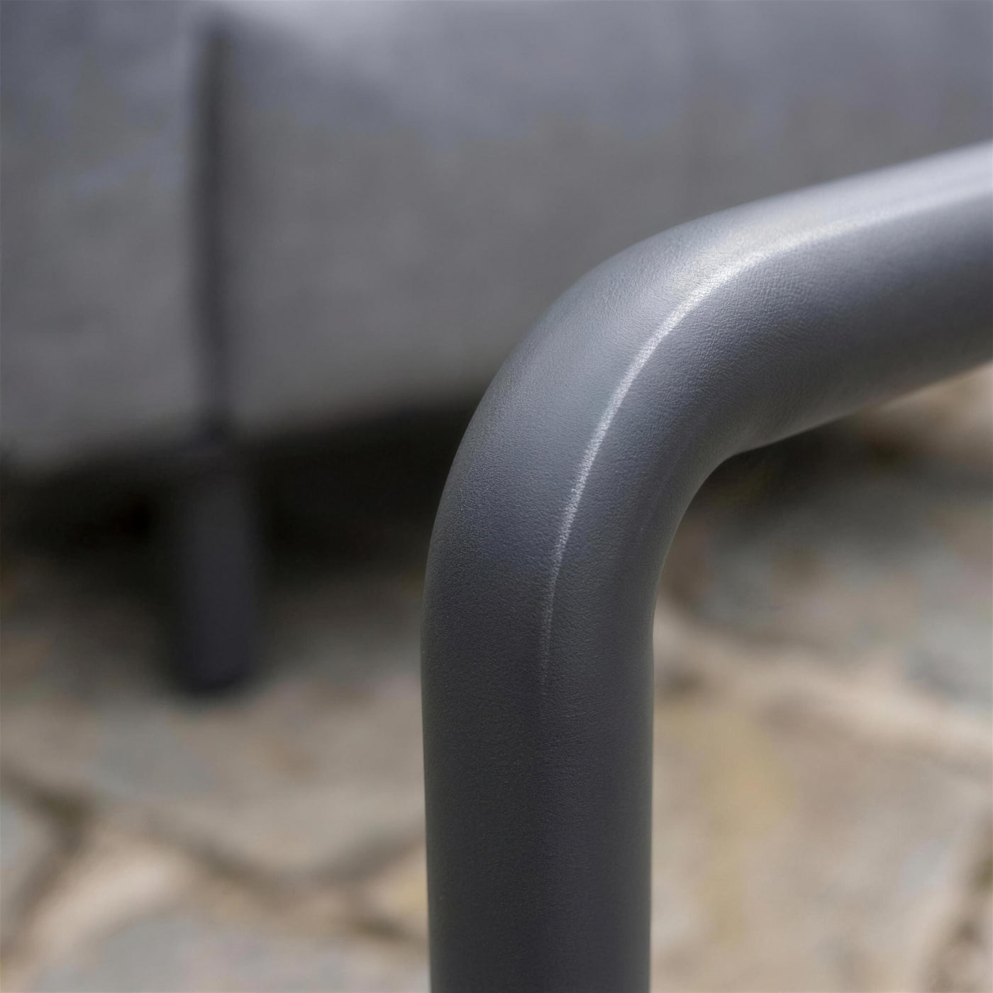Detalle del codo del tubo de aluminio antracita del sillon Brandon, con su lacado mate granulado y el tejido gris desenfocado detras