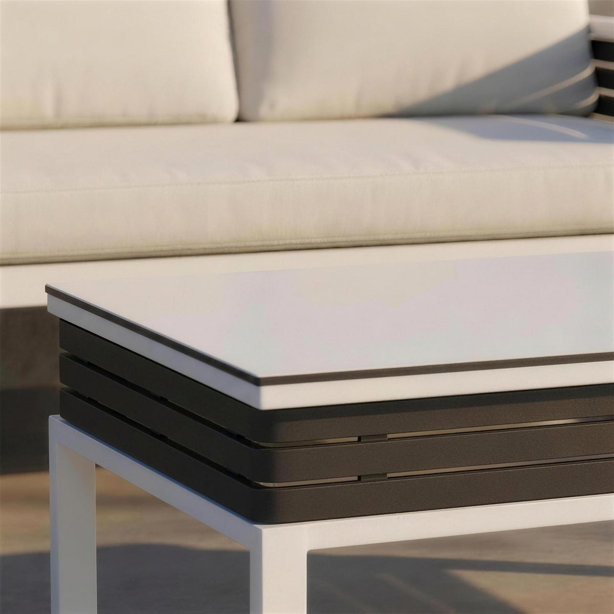 Detalle del canto del tablero blanco encajado sobre las lamas de aluminio antracita de la mesa de centro, con luz rasante de tarde